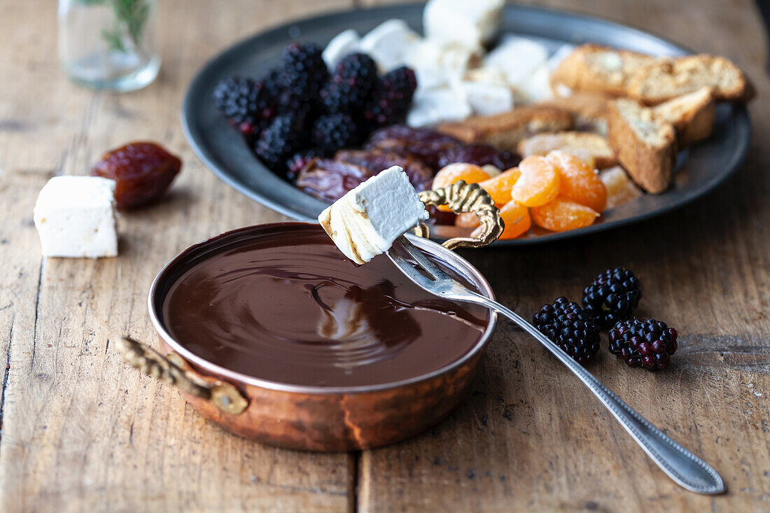 Chocolate fondue with marshmallows and a plate of fruit in the background