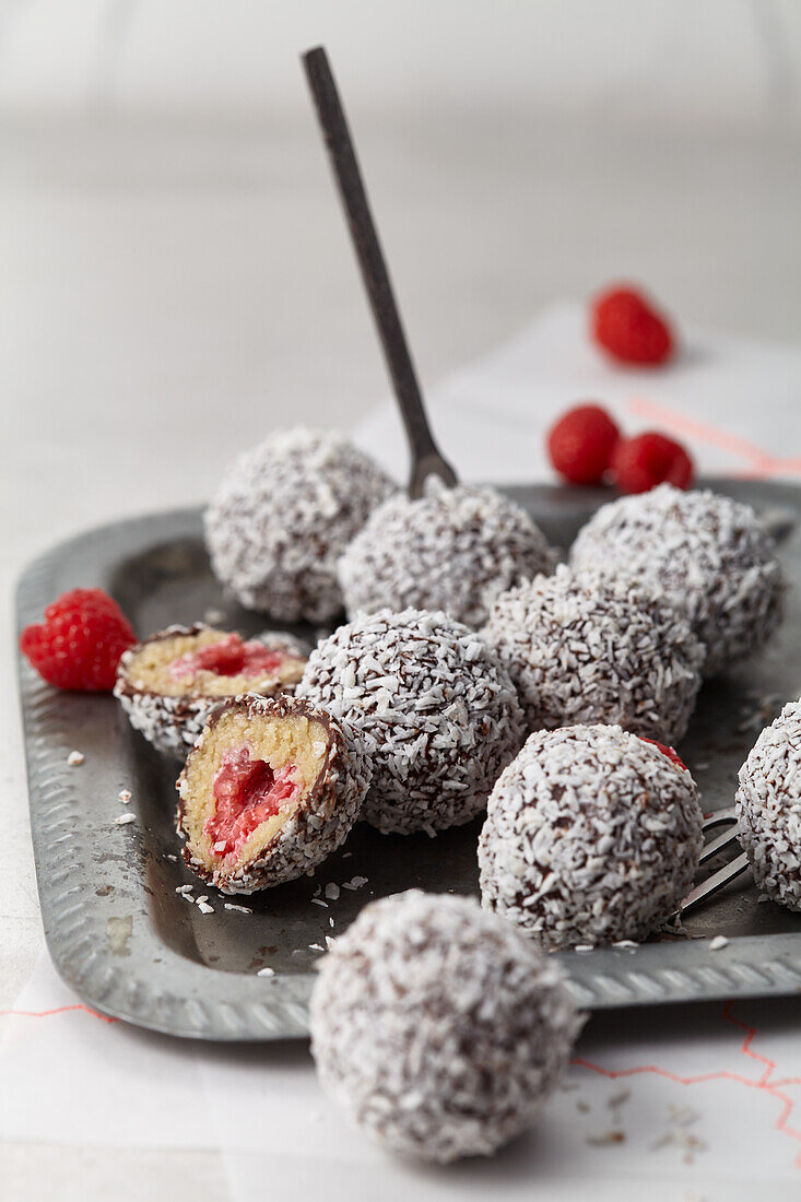 Cashew lamington balls filled with raspberries, dipped in chocolate and coated with coconut flakes