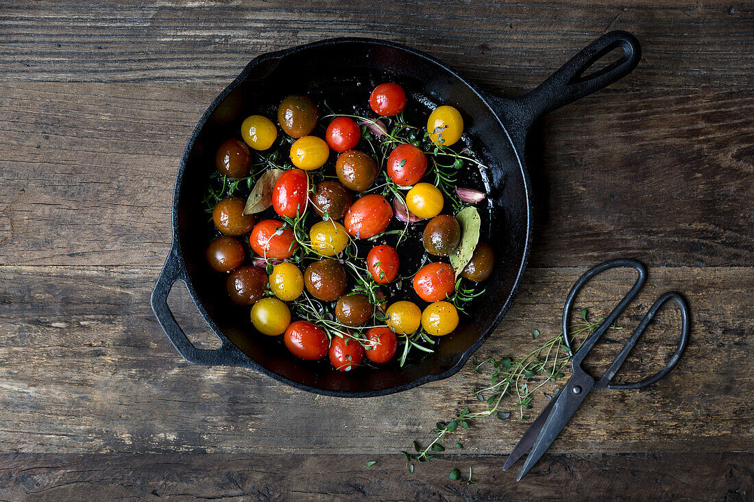 Mixed varieties of tomatoes in a skillet with thyme, rosemary, garlic cloves, bay leaves