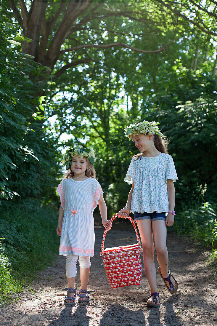 Girls wearing elderflower wreaths carrying a picnic basket