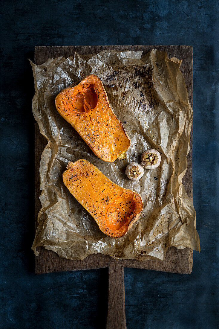 Roasted butternut squash halves and whole garlic heads on baking pape