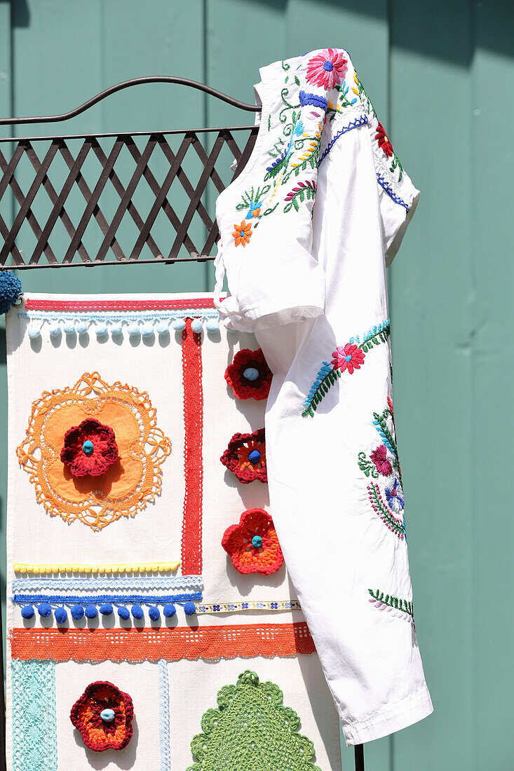 Screen decorated with doilies, trims, crochet flowers and pompoms with embroidered dress hung on corner