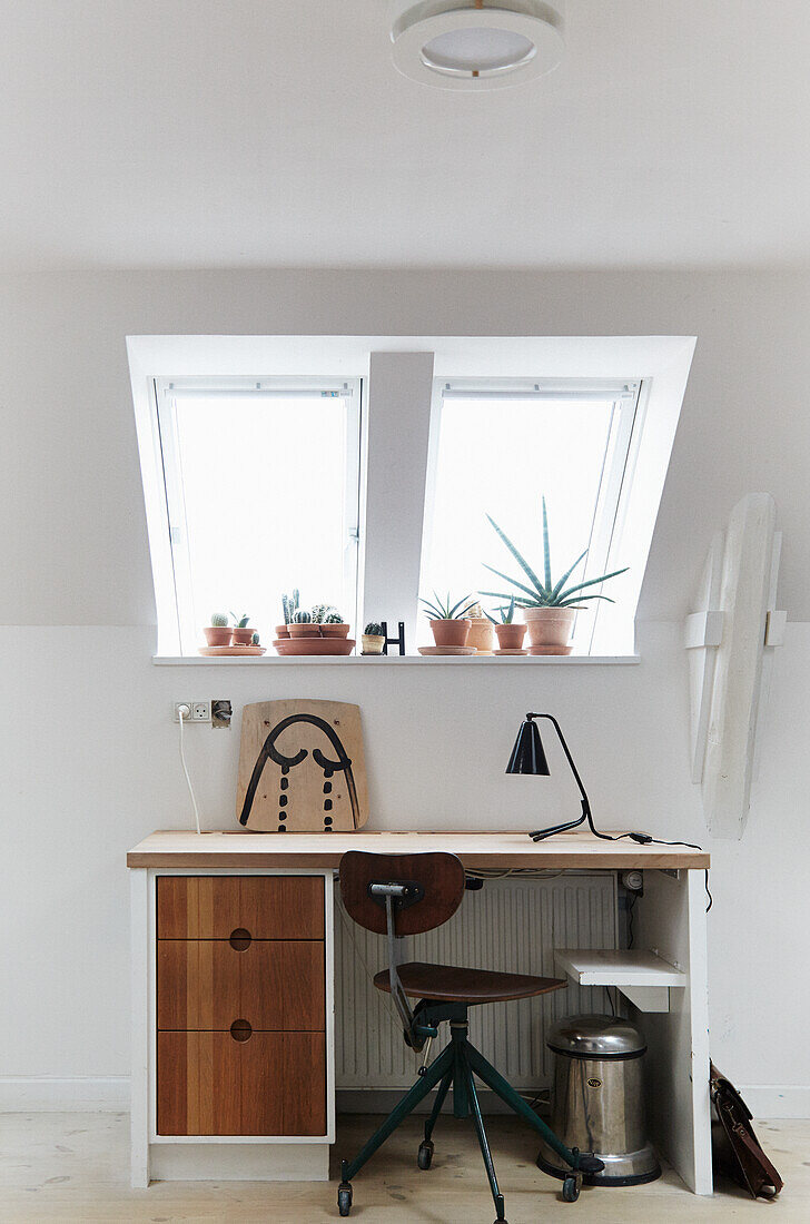 Arbeitsplatz unter Dachschräge mit Vintage-Schreibtisch und Zimmerpflanzen auf der Fensterbank