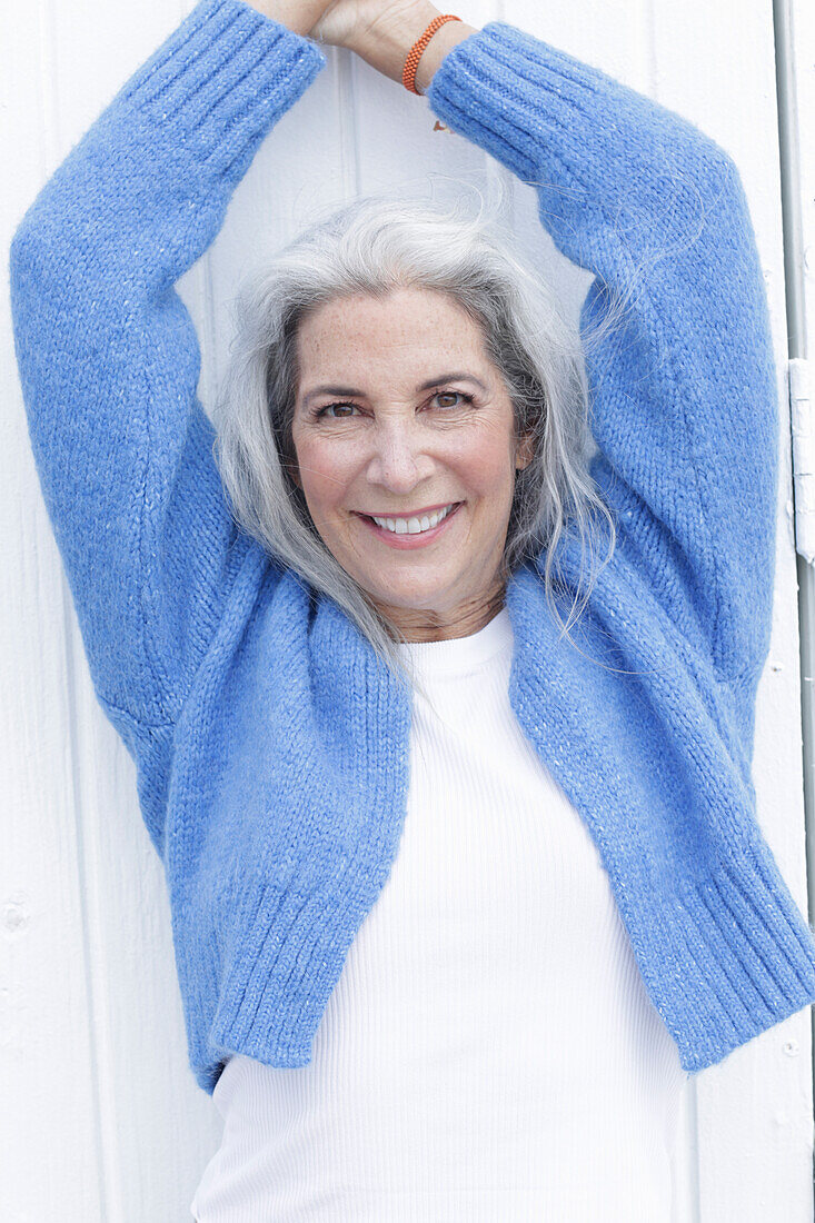 A mature woman with grey hair wearing a white t-shirt and a blue cardigan