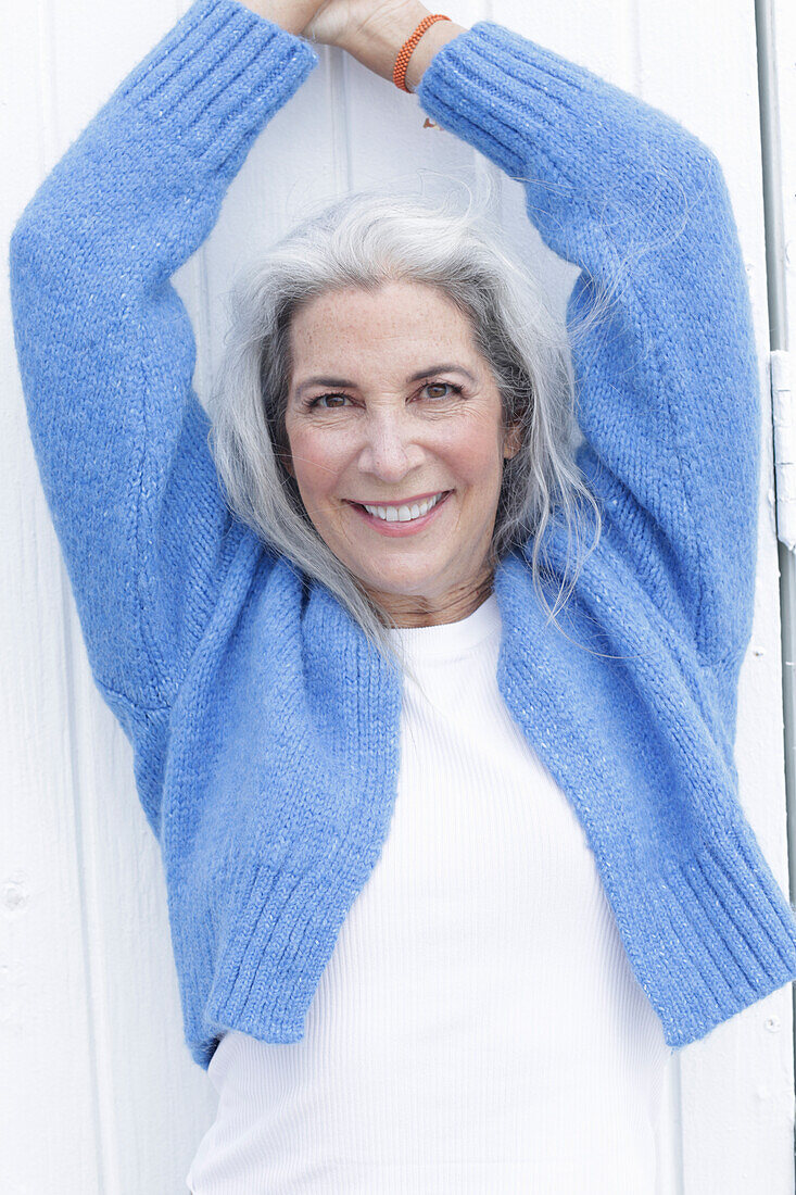 Reife Frau mit grauen Haaren in weißem T-Shirt und blauer Strickjacke