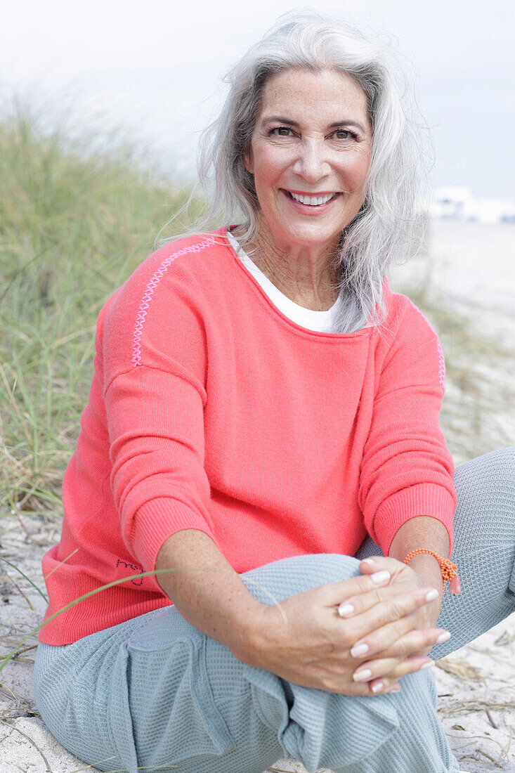 Mature woman with grey hair in salmon-coloured jumper and trousers on the beach