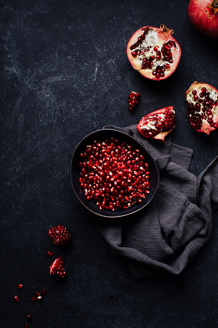 Broken open pomegranate and bowl with pomegranate seeds on dark background