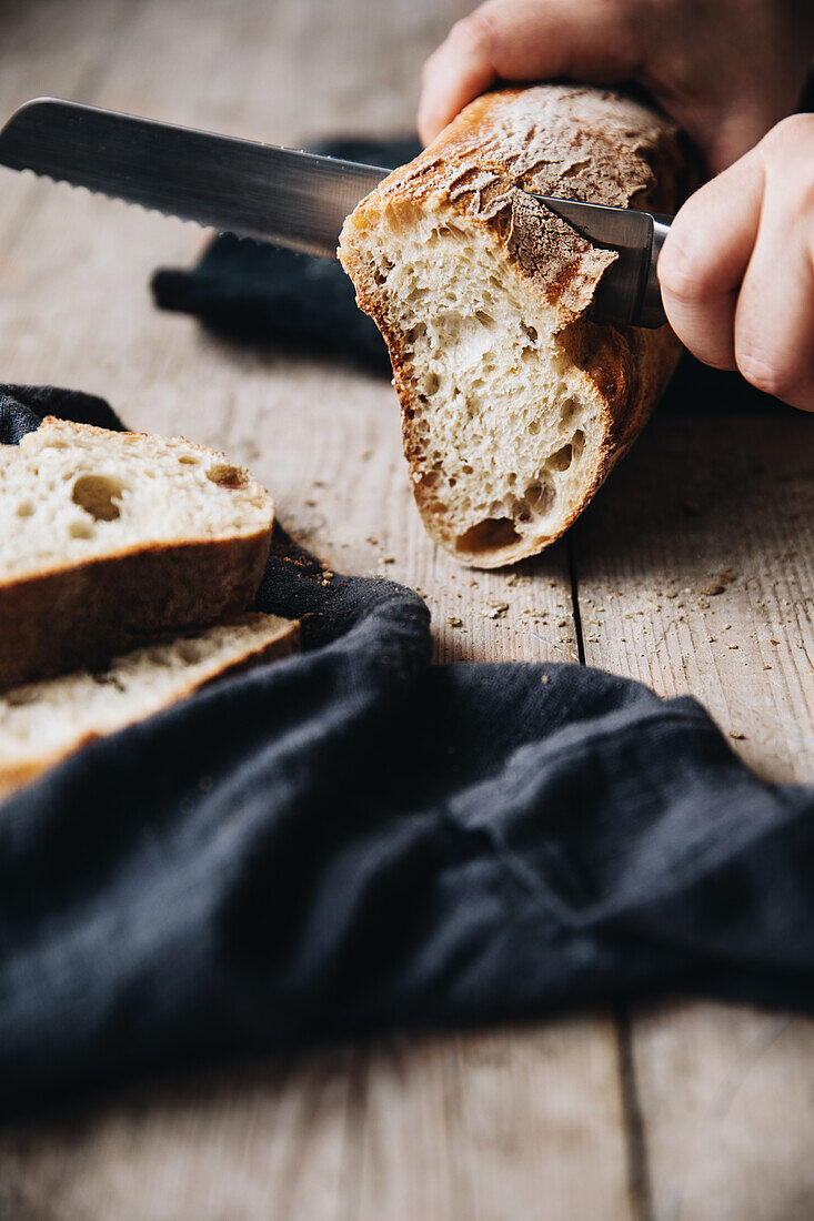 Baguette schneiden, im Vordergrund schwarzes Leinentuch auf Holztisch