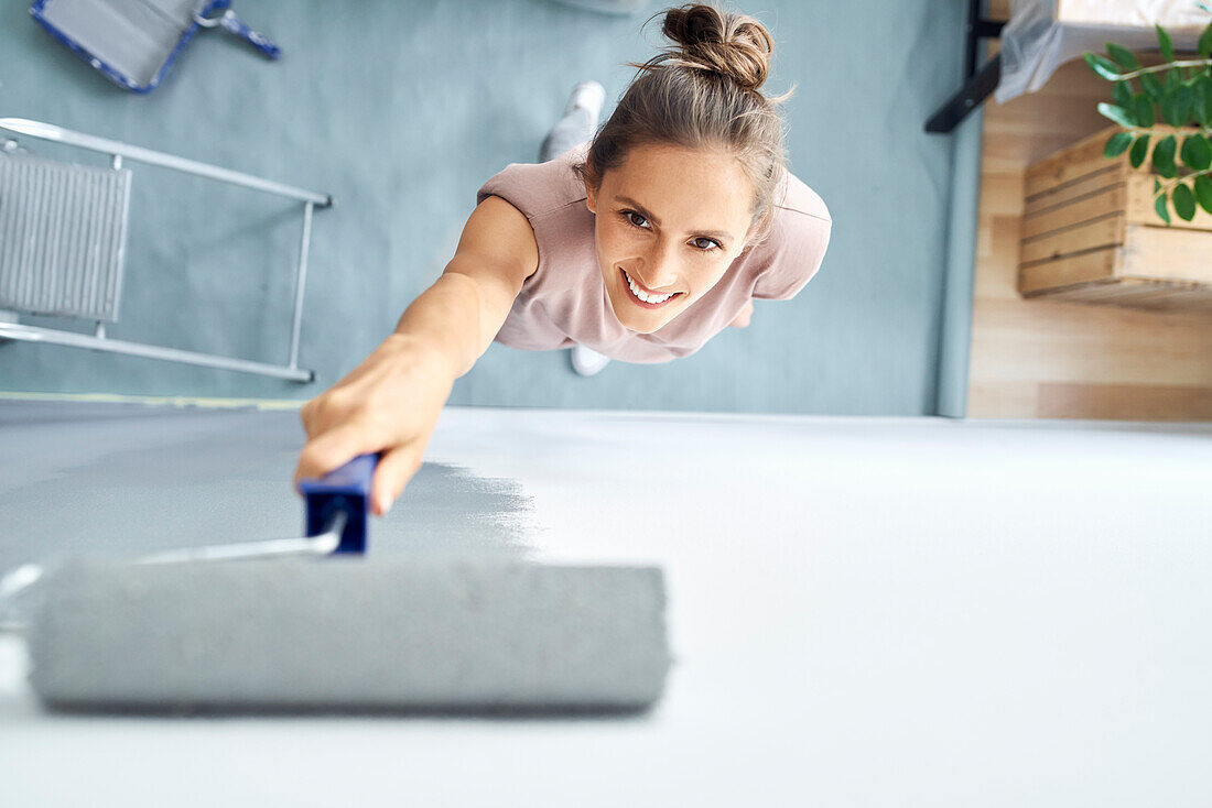 Smiling young woman painting wall with paint roller