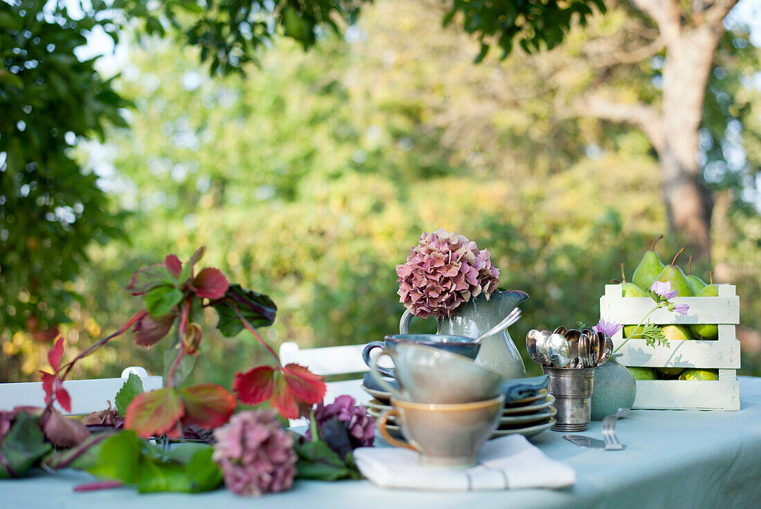 Crockery, DIY lamp shade and jug with blooming hydrangeas lying on coffee table set in garden