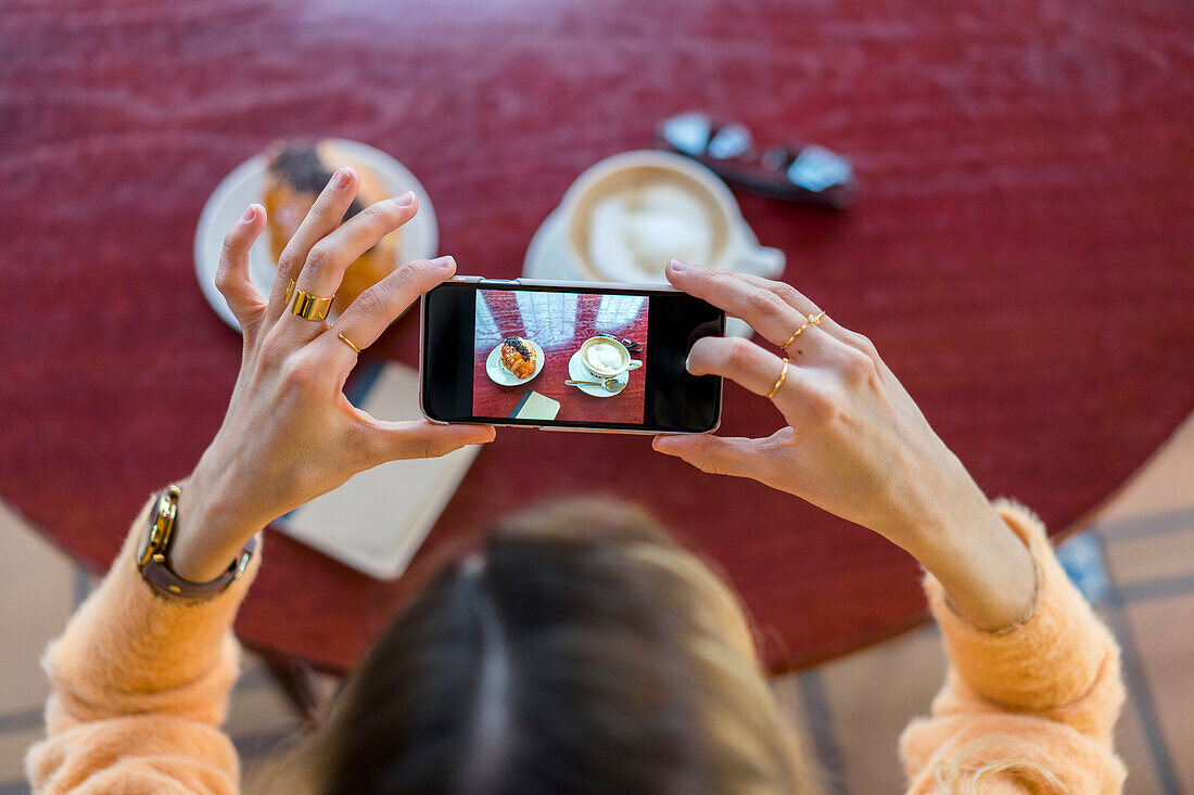 Draufsicht einer Frau in einem Café, die ein Handyfoto macht