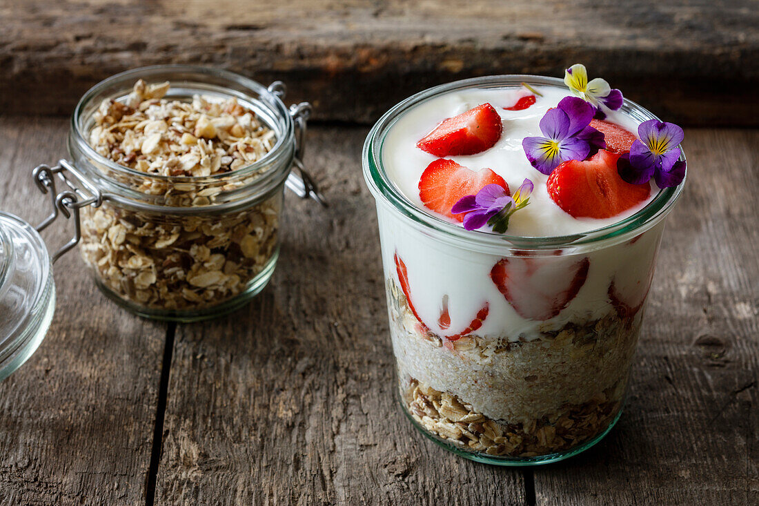 Glass of granola with natural yogurt, strawberries and Horned Violets