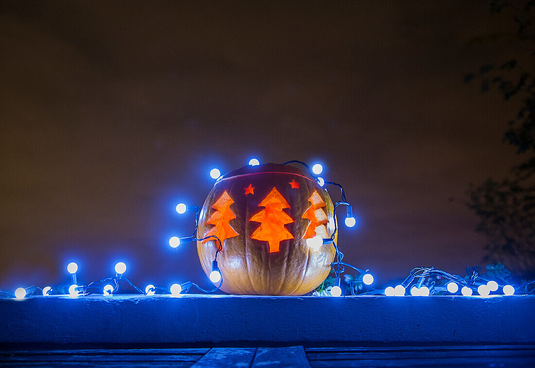 Jack o lantern decorated with blue Christmas lights glowing outdoors at night