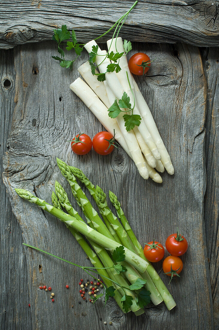 Green and white asparagus, parsley, tomatoes and mixed peppercorns on wood