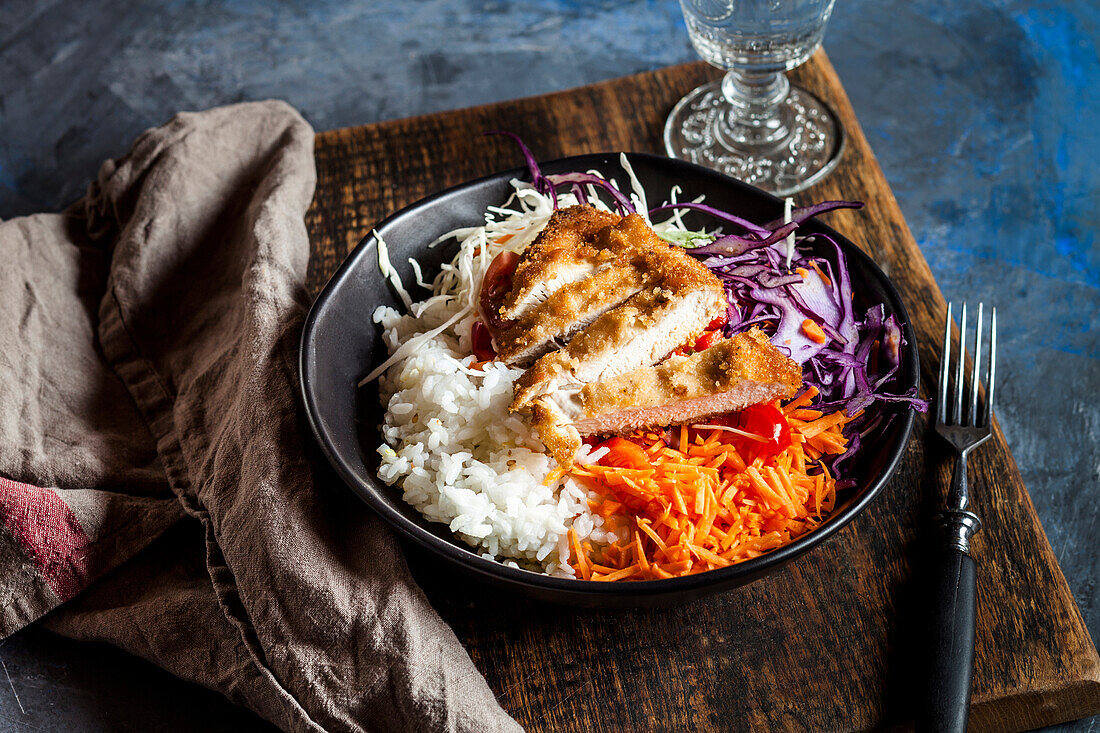 Bowl of ready-to-eat salad with white and red cabbage, carrots, rice and chicken schnitzel