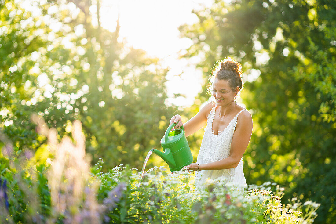 Junge Frau, die Blumen im Frühlingsgarten gießt