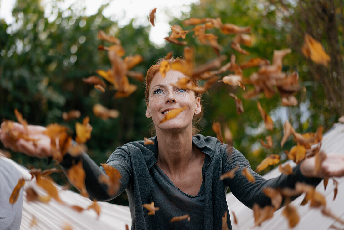 Sorglose Frau in der Hängematte, die Herbstblätter wirft