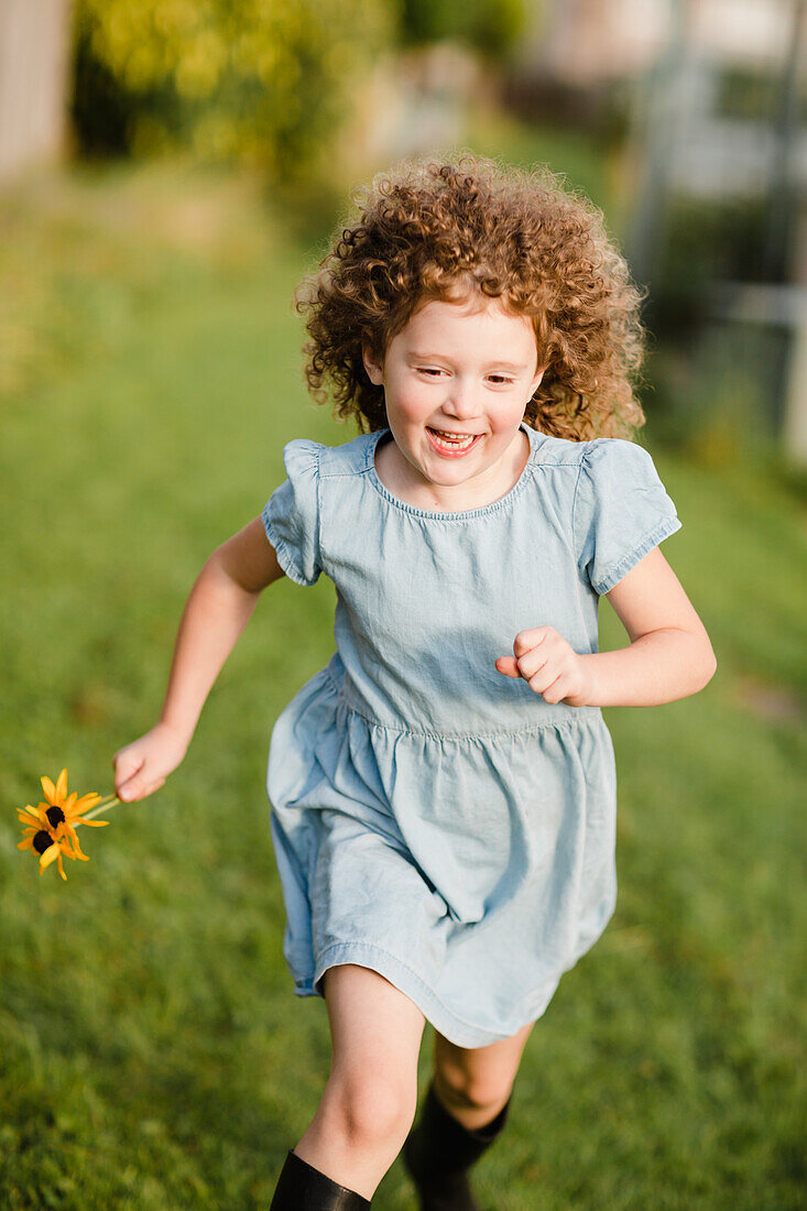 Glückliches kleines Mädchen, das auf einer Wiese im Garten läuft