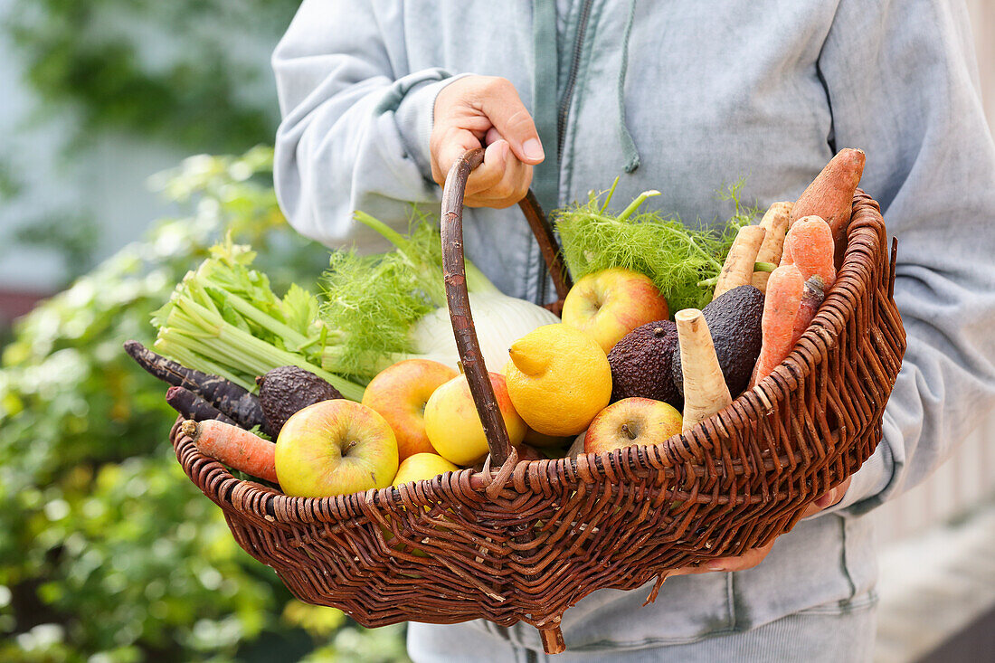 Hand holding a basket with fresh vegetables and fruit