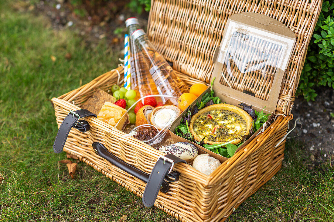 Picknickkorb mit Quiche, Salat, Brötchen und Obst