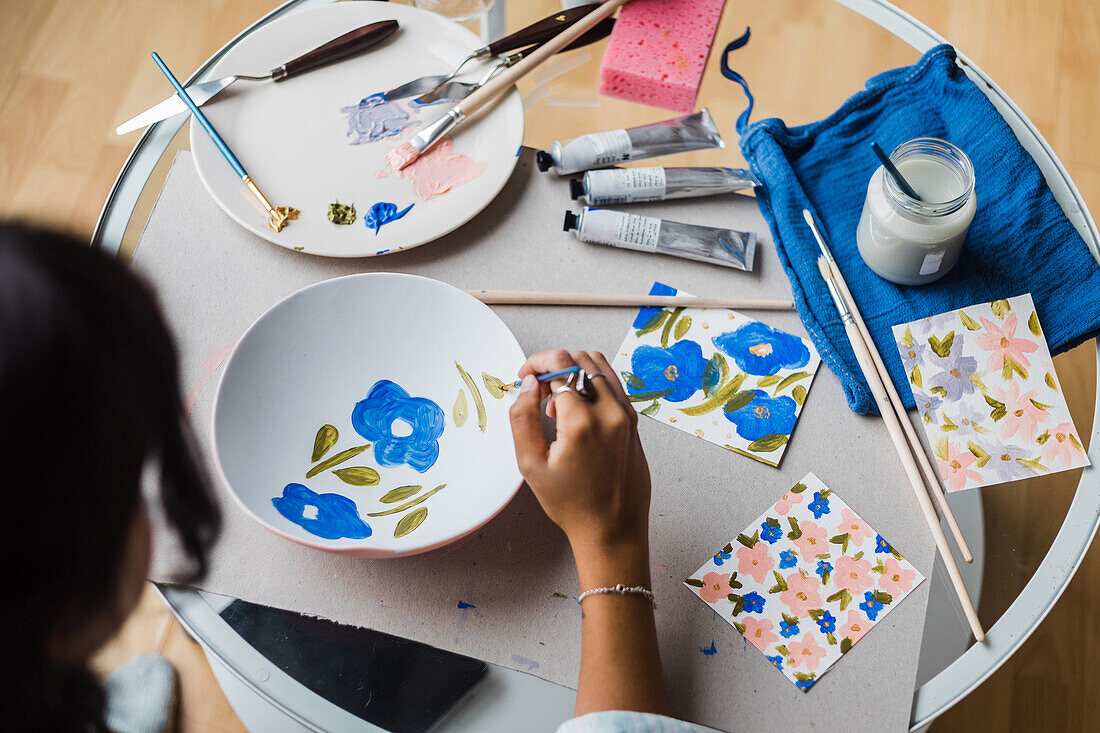 Frau bemalt weißen Keramikteller mit Blumenmotiv