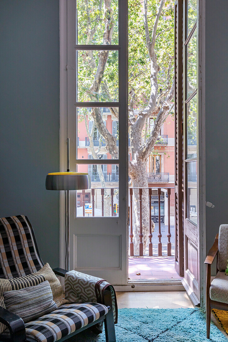 Armchair with chequered upholstery next to balcony door in period apartment