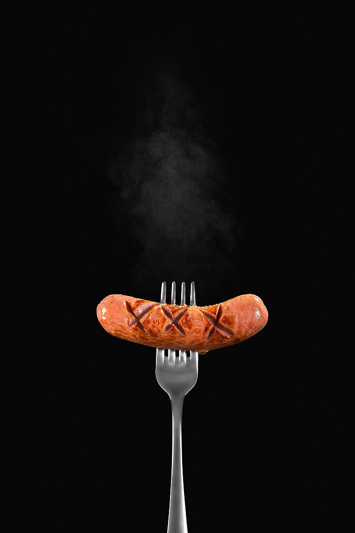 A hot sausage on a fork against a black background
