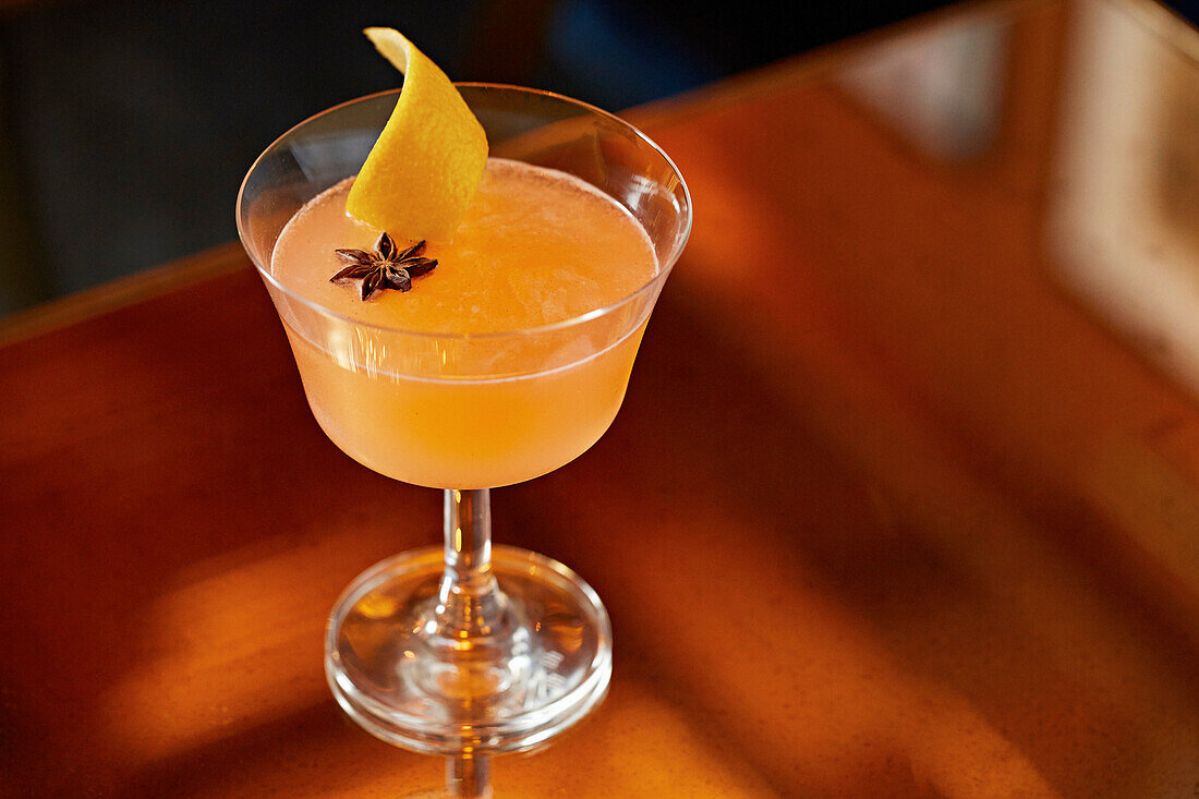 An orange cocktail garnished with star anise and lemon