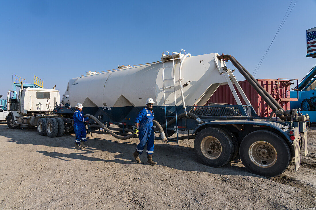 Oilfield workers unloading a hose to transfer dry cement