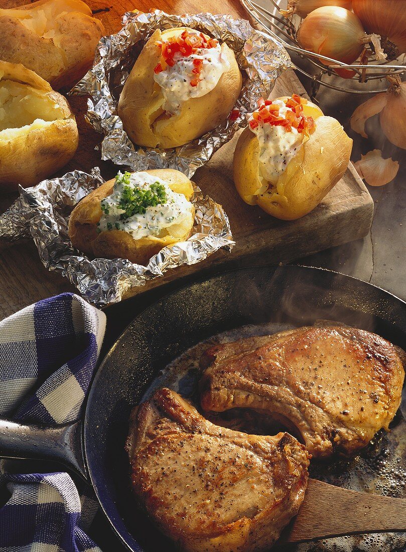 Pork cutlets in pan & baked potatoes on wooden board