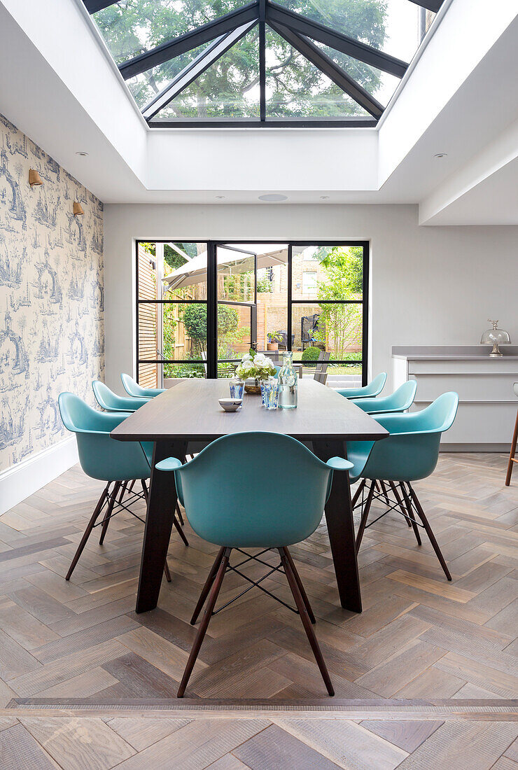 Dining area with glass ceiling, turquoise-colored chairs and view of the garden