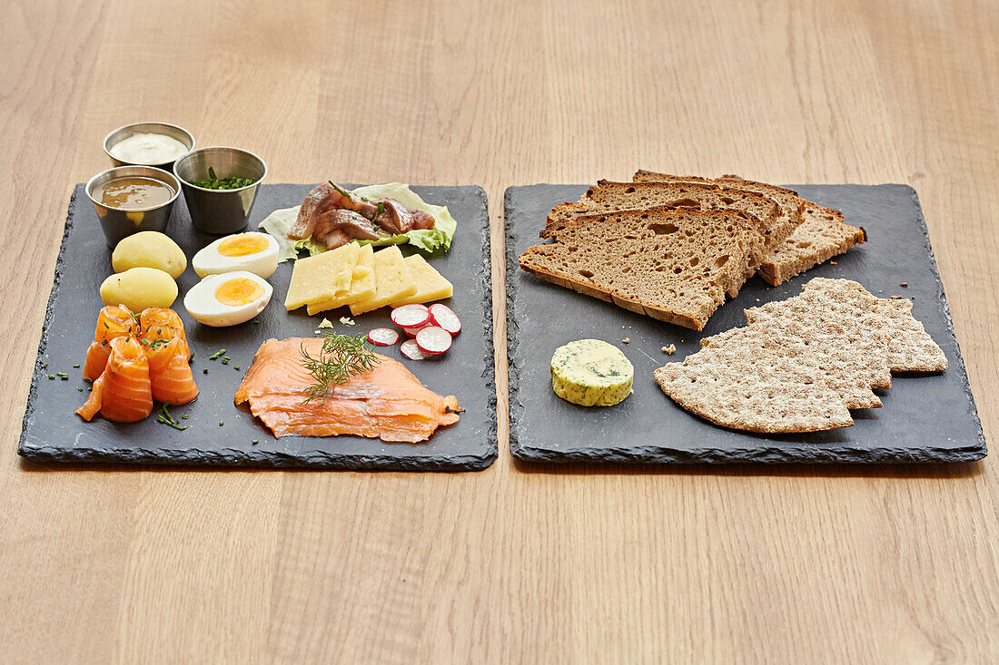 Lachs, Eier, Käse, Salat und frisches Brot serviert auf Schieferplatten
