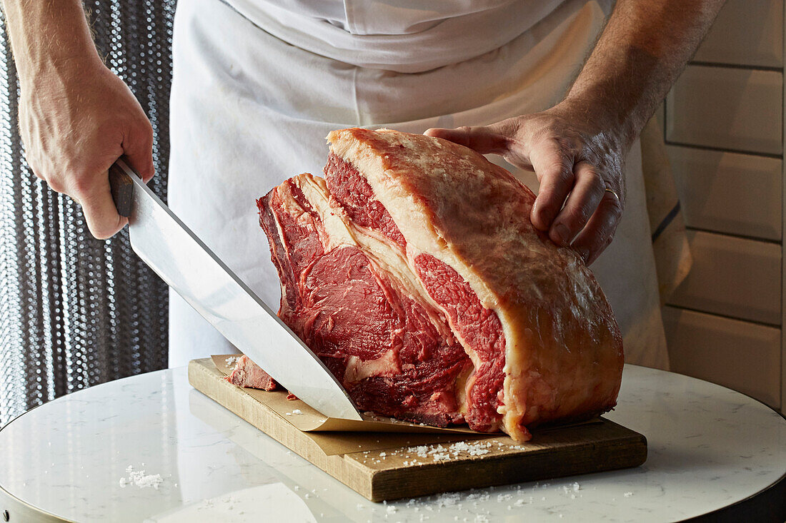 A forerib of beef on the butchers block with a chef and knife