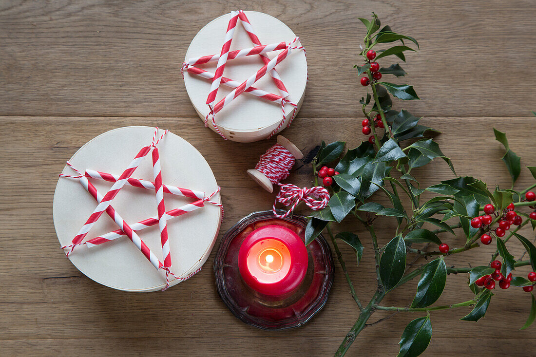 Weihnachtliche Tischdekoration mit roter Kerze, Stechpalmen und DIY-Schachteln mit Sternen