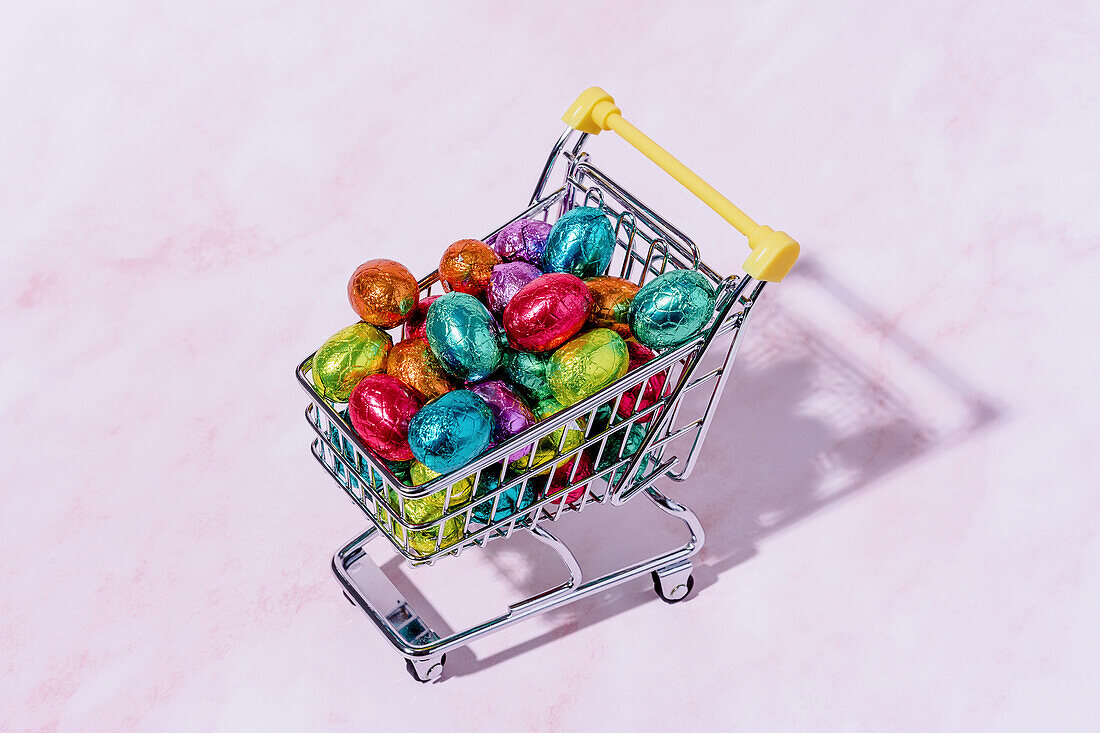A shopping cart with colourful chocolate eggs on a pink background