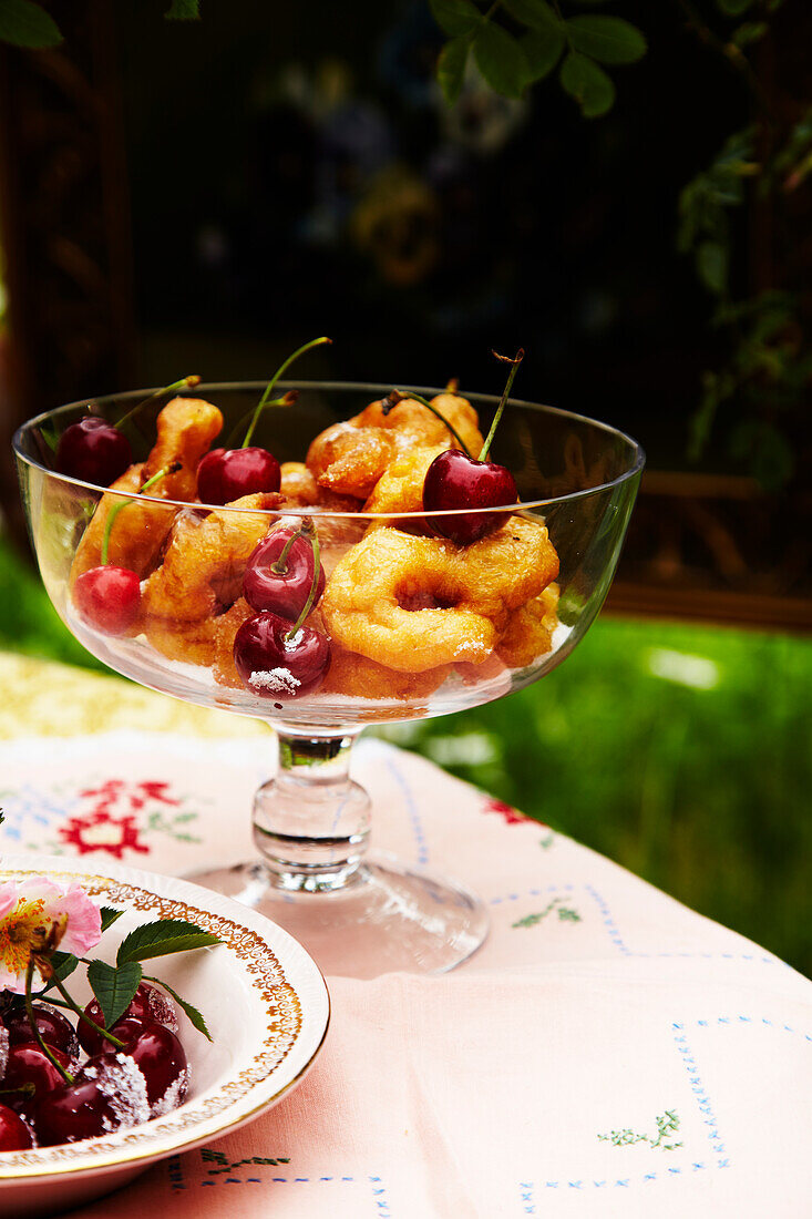 Italienisches frittiertes Gebäck mit Kirschen in Glasgefäß auf Tisch im Garten