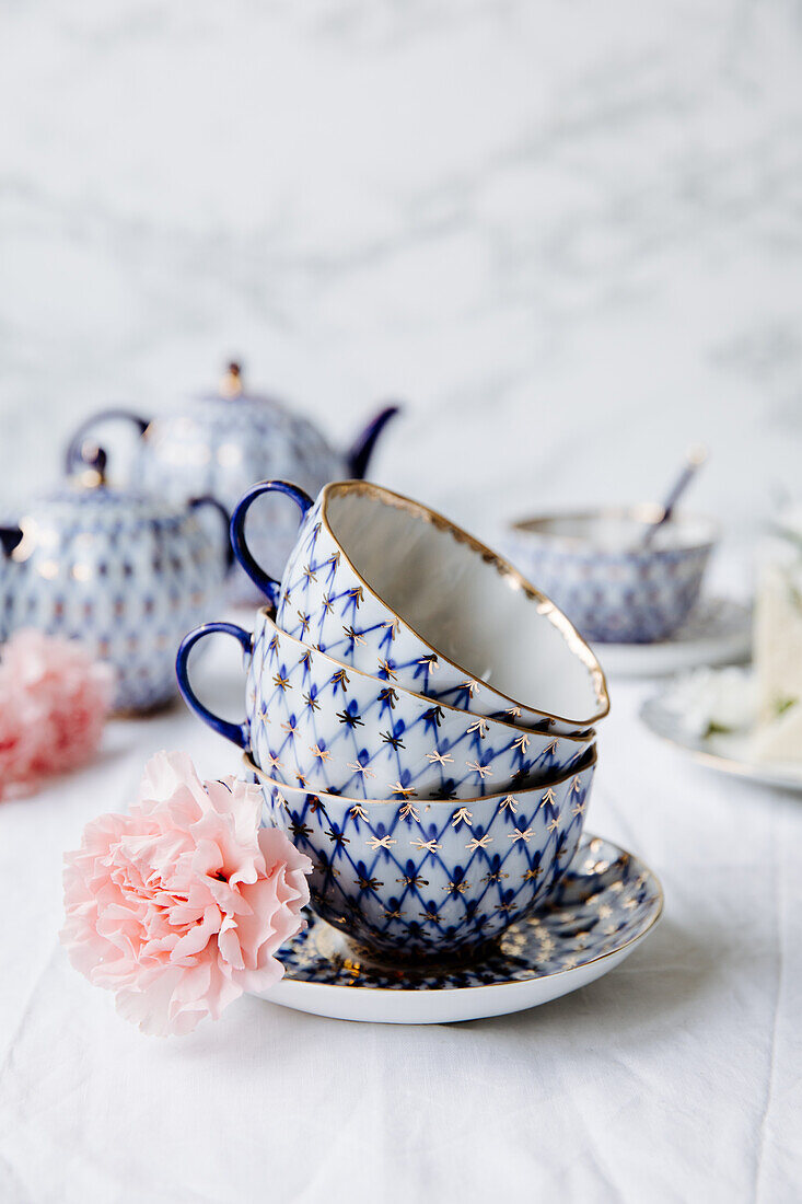 Decorative teacups with a blue-golden net pattern next to a clove blossom