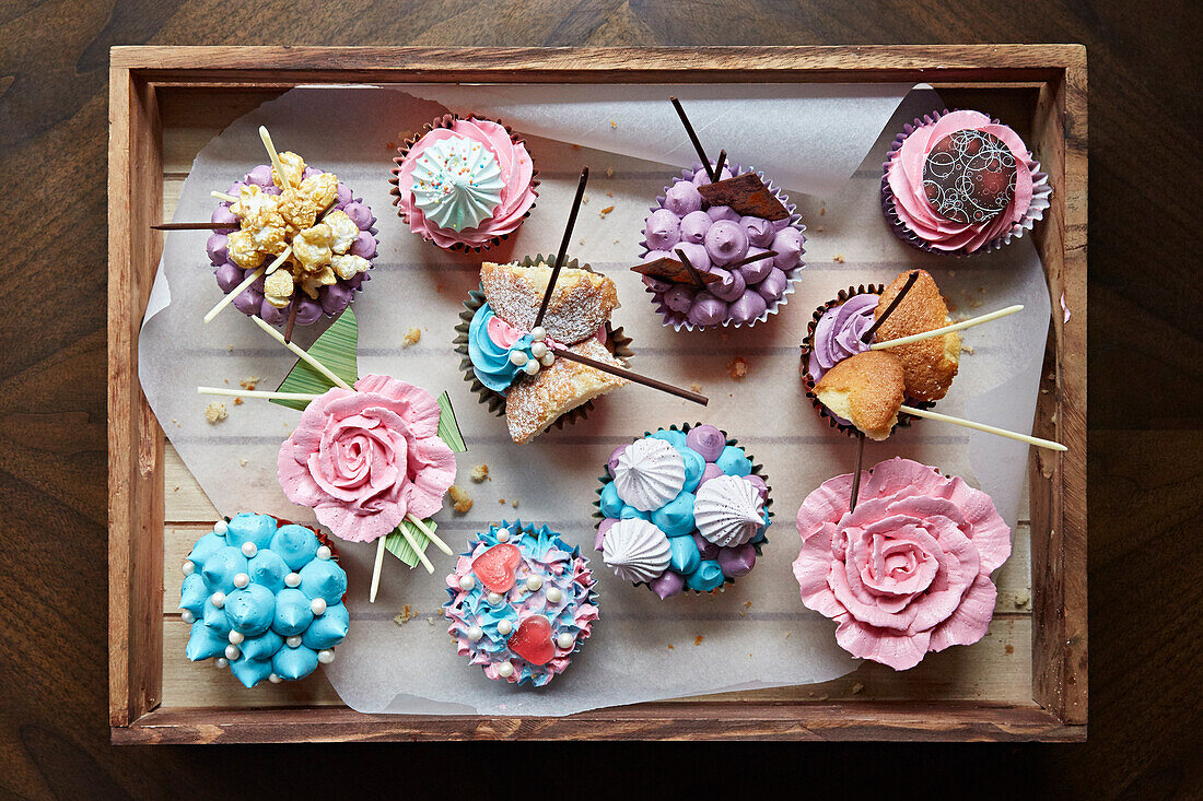 Verschiedene aufwendig verzierte Cupcakes auf Holztablett