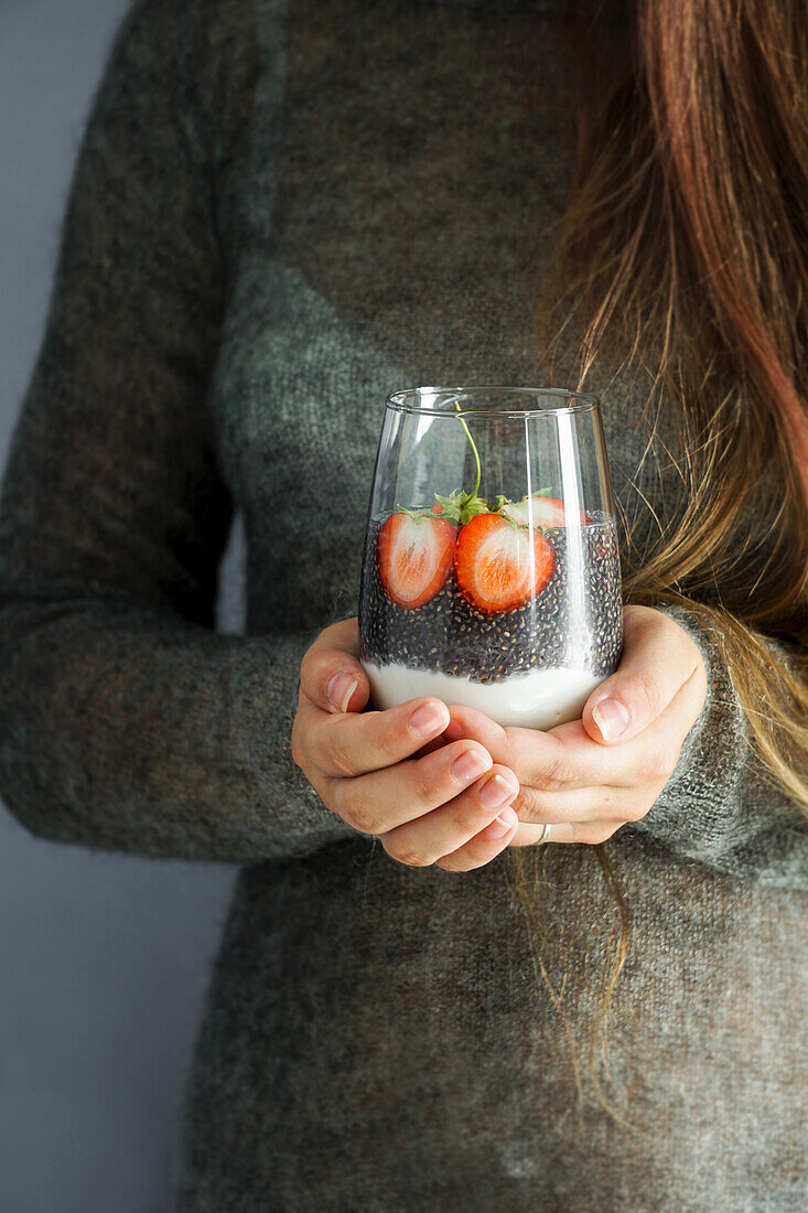 Hände halten Glas mit Chiapudding, Joghurt und Erdbeeren