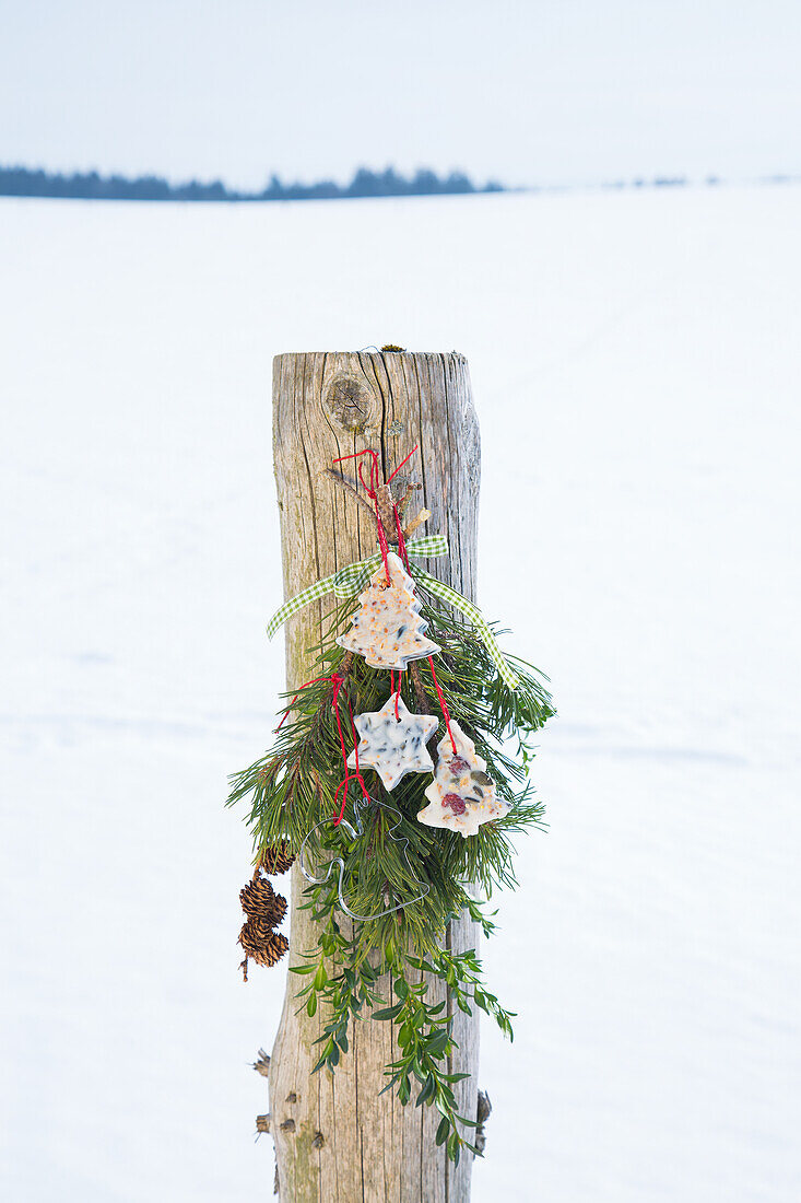 Winterliche Dekoration mit Vogelfutter an Holzpfahl im Schnee