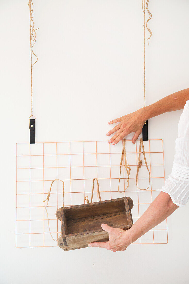 Attaching a wooden box to a copper wall grid with strings