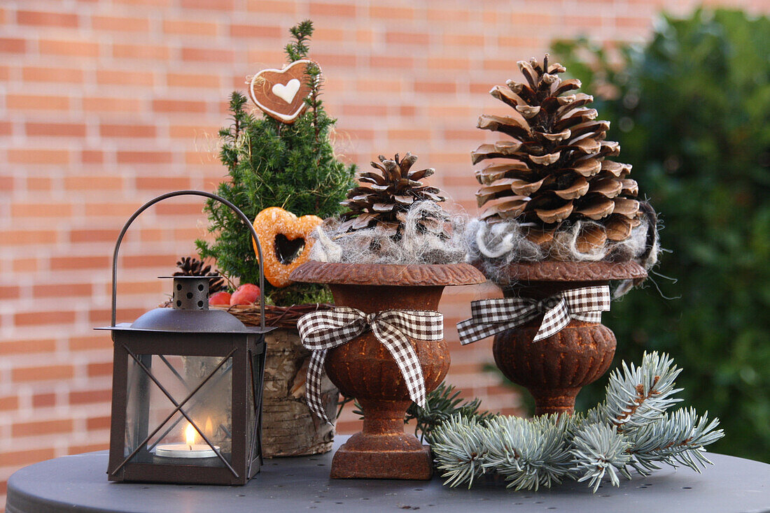 Pine cones in rusty urns and little tree decorated for Christmas next to candle lantern