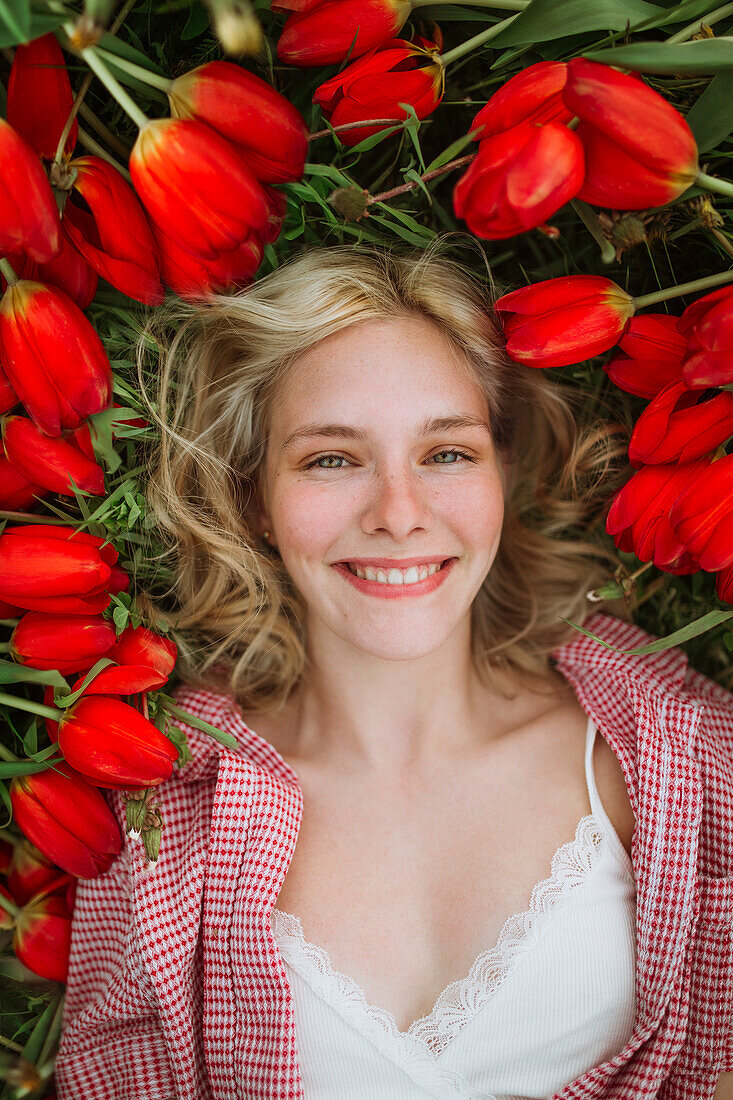 Junge blonde Frau umgeben von roten Tulpen liegt auf einer Wiese