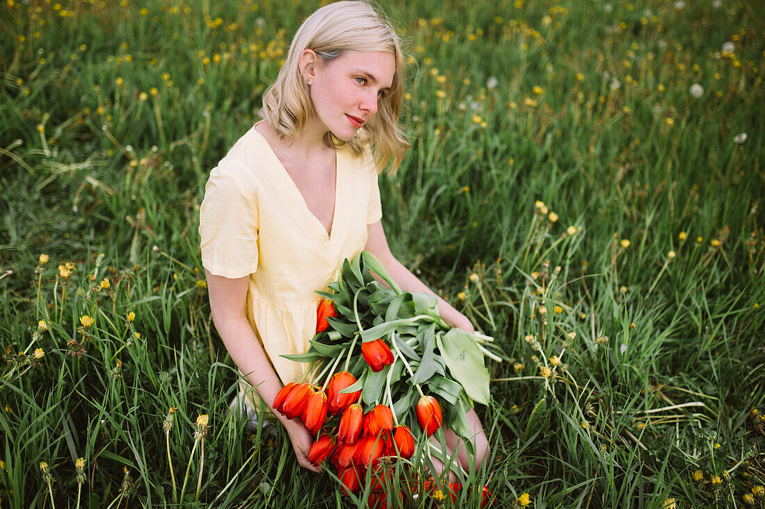 Content female in dress standing with bunch of red tulip flowers in meadow in summer