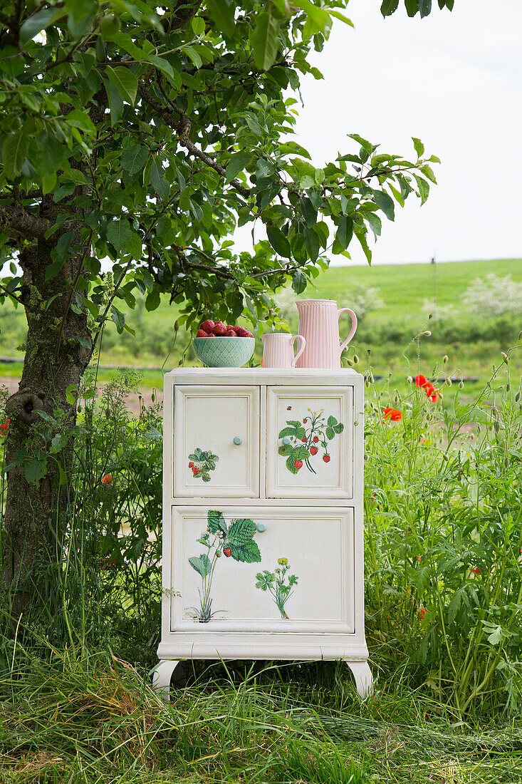 An upcycled bedside table with a strawberry design in a garden
