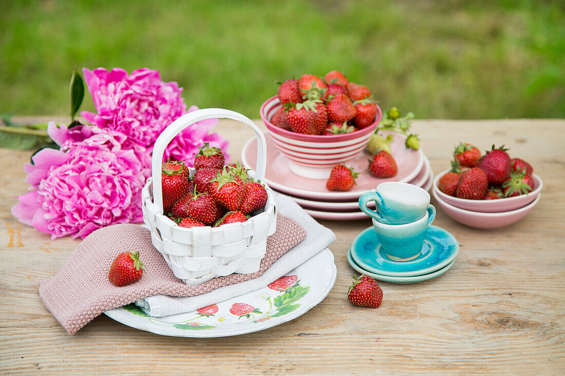 Fresh strawberries, dishes and peonies on a garden table