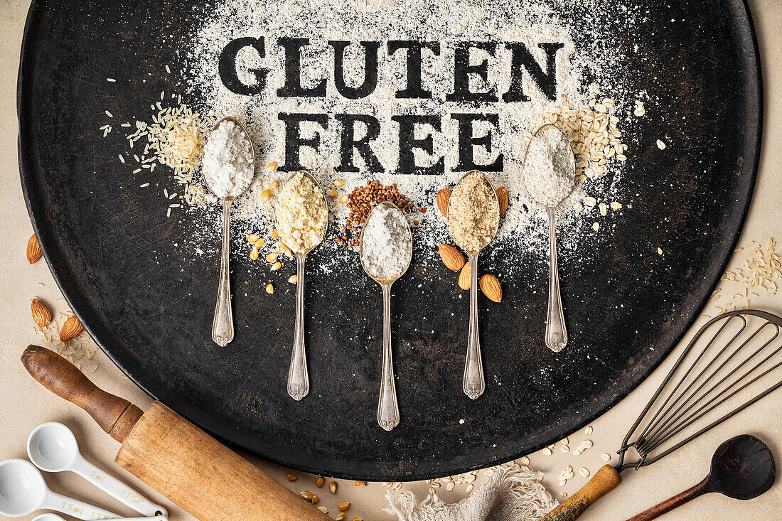 Gluten free written in flour on vintage baking sheet, kitchen utensils and spoons of various gluten free flour