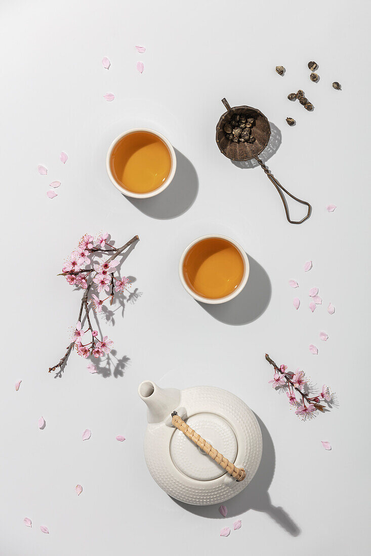 Tea concept, two white cups of tea, teapot, tea strainer and spring sakura branches on concrete background,