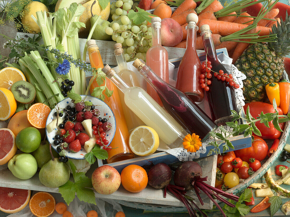 Flaschen mit selbstgemachtem Obstsaft und Gemüsesaft, umgeben von verschiedenen Sorten Obst und Gemüse
