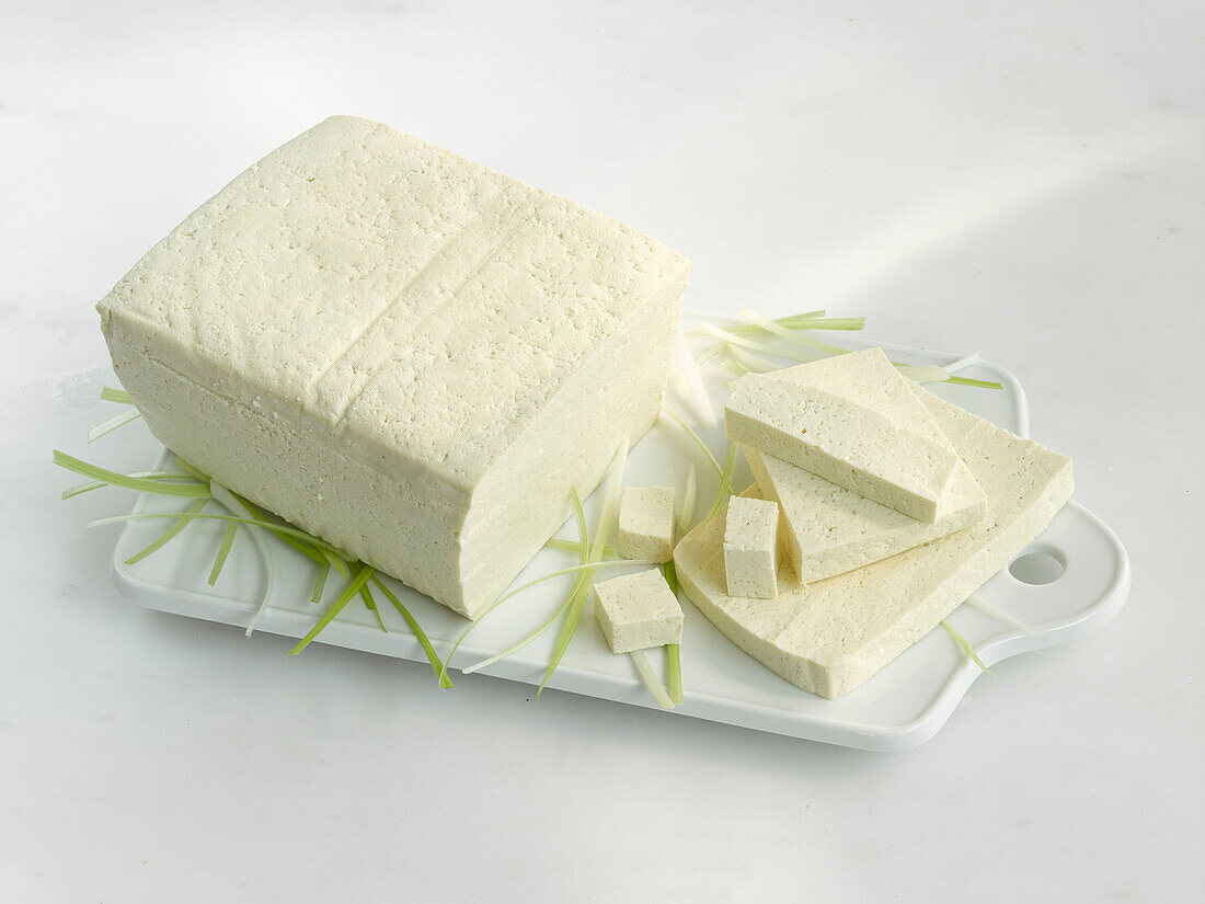 Ein Stück und einige Scheiben Tofu auf weißem Brettchen